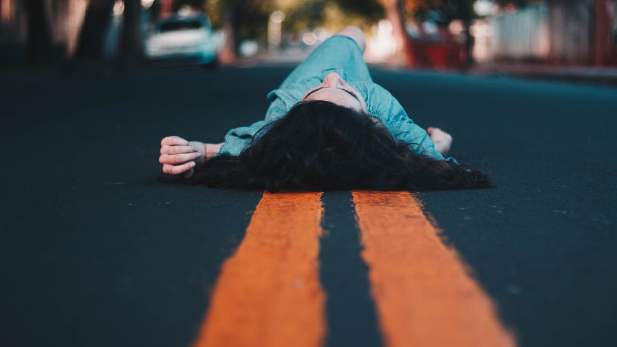 A woman lying on an urban street, surrounded by vibrant colors of nature.